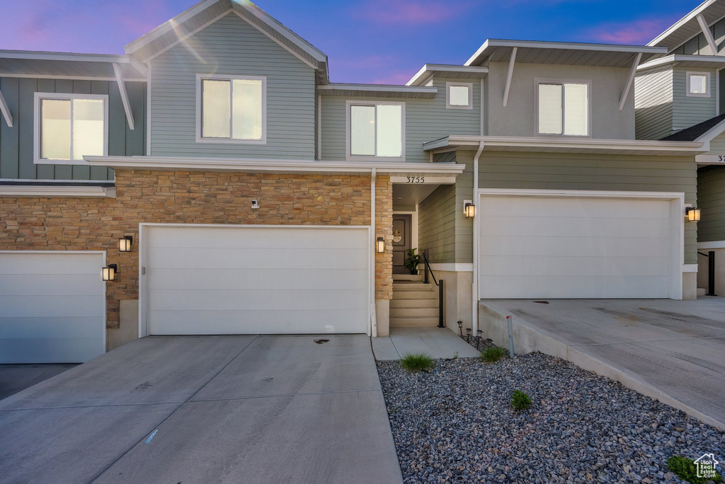View of front facade with a garage, driveway, stone siding, and board and batten siding