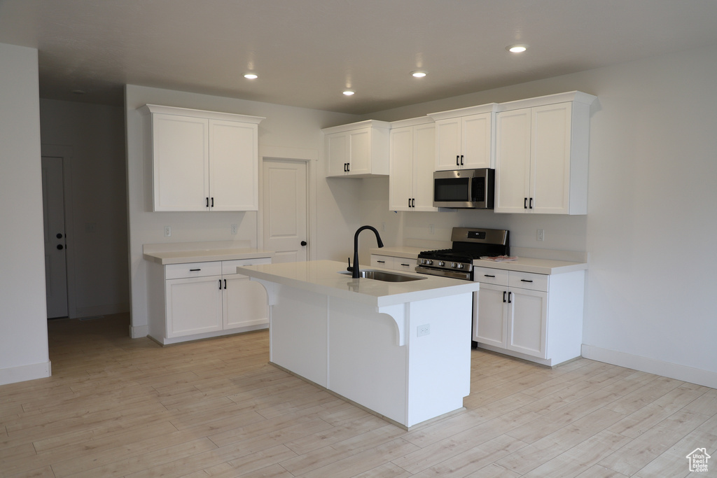 Kitchen featuring appliances with stainless steel finishes, a sink, light countertops, an island with sink, and light wood-style flooring