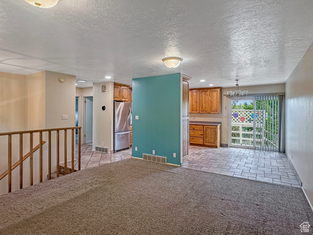 Unfurnished living room with a chandelier, a textured ceiling, light carpet, recessed lighting, and baseboards