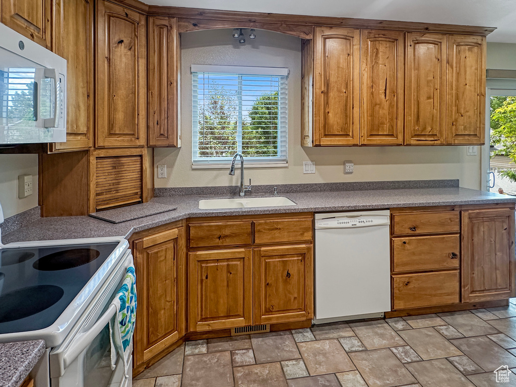 Kitchen featuring white appliances, a sink, brown cabinetry, and stone finish flooring