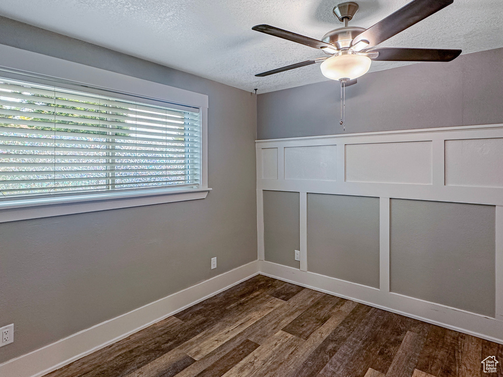 Unfurnished room with dark wood finished floors, a textured ceiling, a decorative wall, a ceiling fan, and a wainscoted wall
