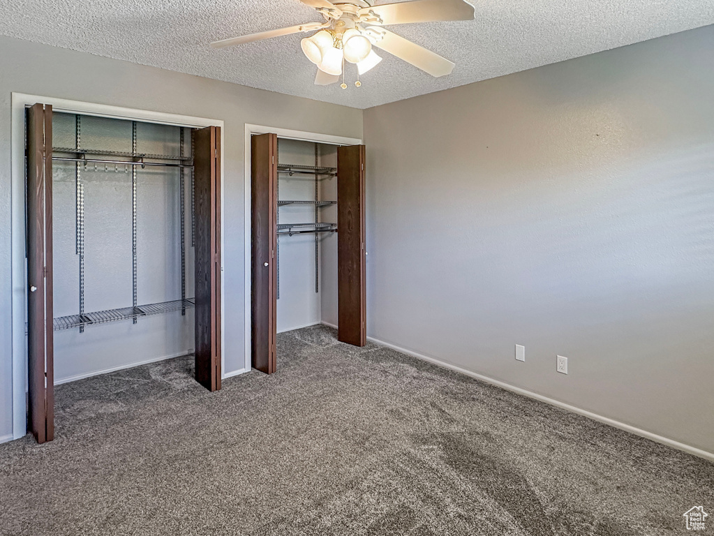 Unfurnished bedroom with carpet, two closets, a textured ceiling, baseboards, and a ceiling fan