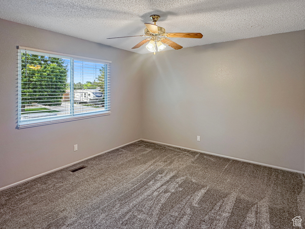 Carpeted spare room with ceiling fan, a textured ceiling, and baseboards