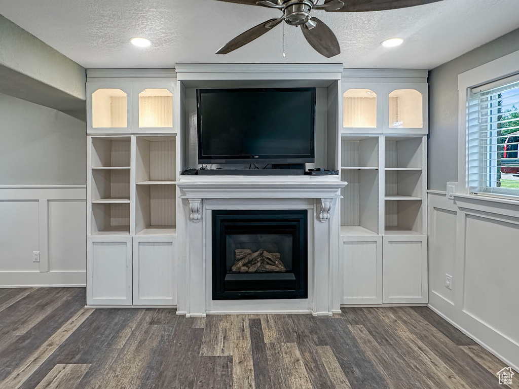 Unfurnished living room with a decorative wall, a fireplace, ceiling fan, wainscoting, and dark wood-style floors
