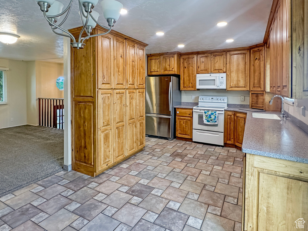 Kitchen featuring white appliances, a sink, a chandelier, brown cabinetry, and baseboards