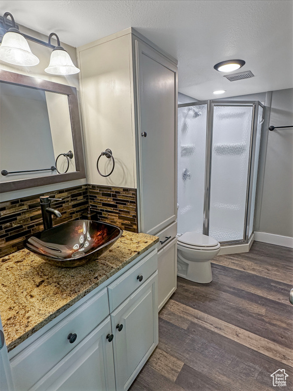 Full bath with a shower stall, wood finished floors, vanity, backsplash, and toilet