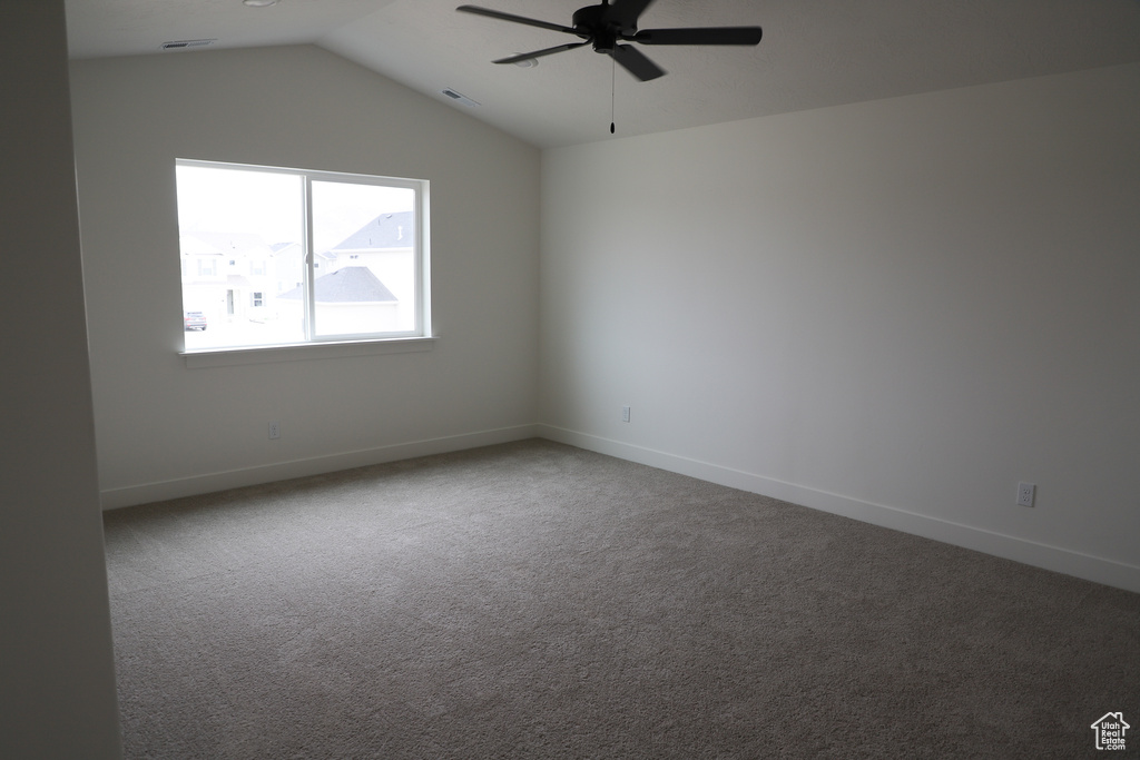 Carpeted empty room with a ceiling fan, lofted ceiling, and baseboards
