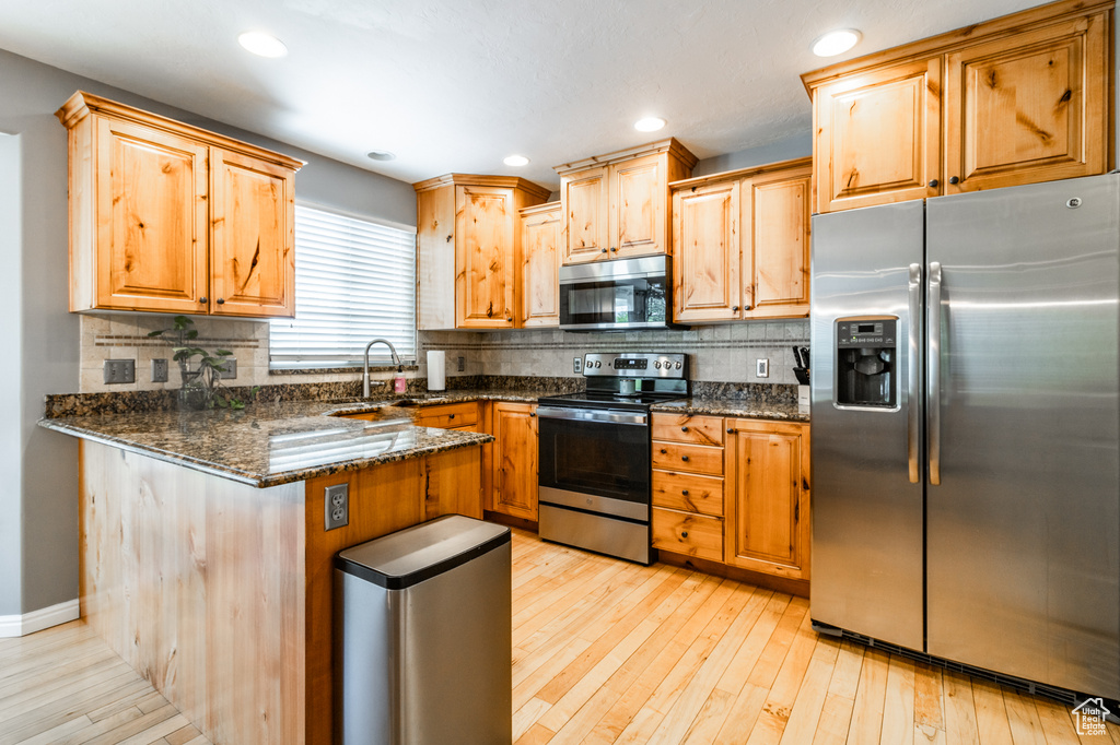 Kitchen featuring appliances with stainless steel finishes, a sink, a peninsula, tasteful backsplash, and light wood-style flooring