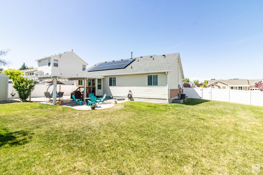 Rear view of property featuring roof mounted solar panels, a patio, roof with shingles, and central AC