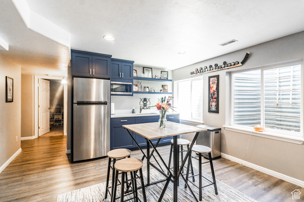 Kitchen with stainless steel appliances, blue cabinetry, light wood finished floors, baseboards, and recessed lighting