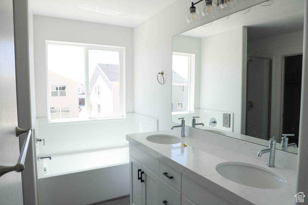 Bathroom featuring healthy amount of natural light, double vanity, a tub to relax in, and a shower