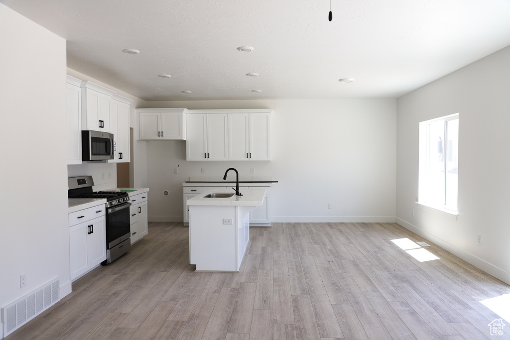 Kitchen with stainless steel appliances, a sink, light wood-type flooring, white cabinetry, and recessed lighting