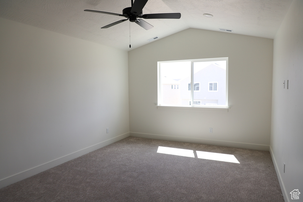 Carpeted spare room with ceiling fan, vaulted ceiling, and baseboards
