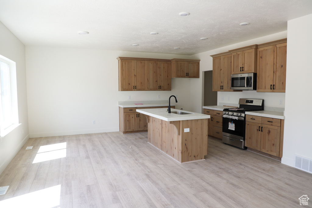 Kitchen featuring stainless steel appliances, a sink, light wood finished floors, light countertops, and brown cabinetry