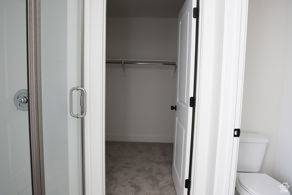 Bathroom featuring a shower with door, toilet, baseboards, and a walk in closet