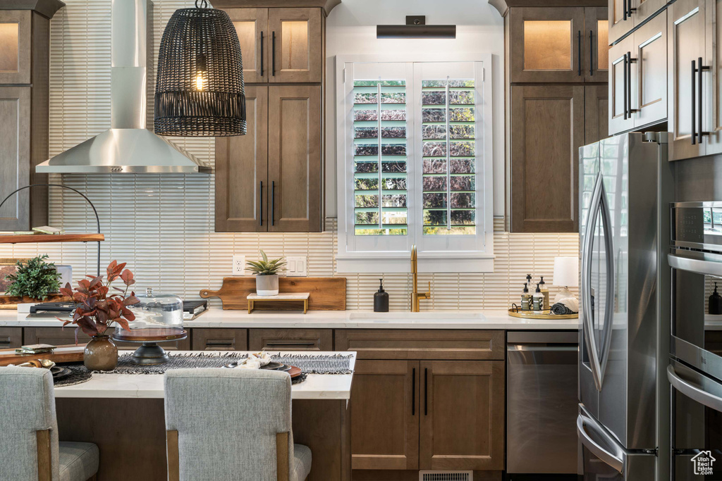 Kitchen with appliances with stainless steel finishes, wall chimney exhaust hood, a sink, backsplash, and light countertops