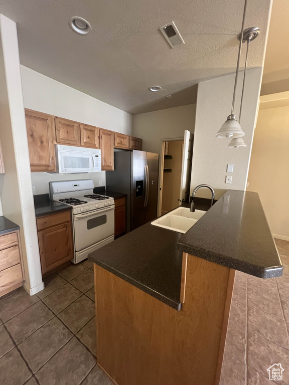 Kitchen with white appliances, a sink, dark countertops, a peninsula, and a textured ceiling