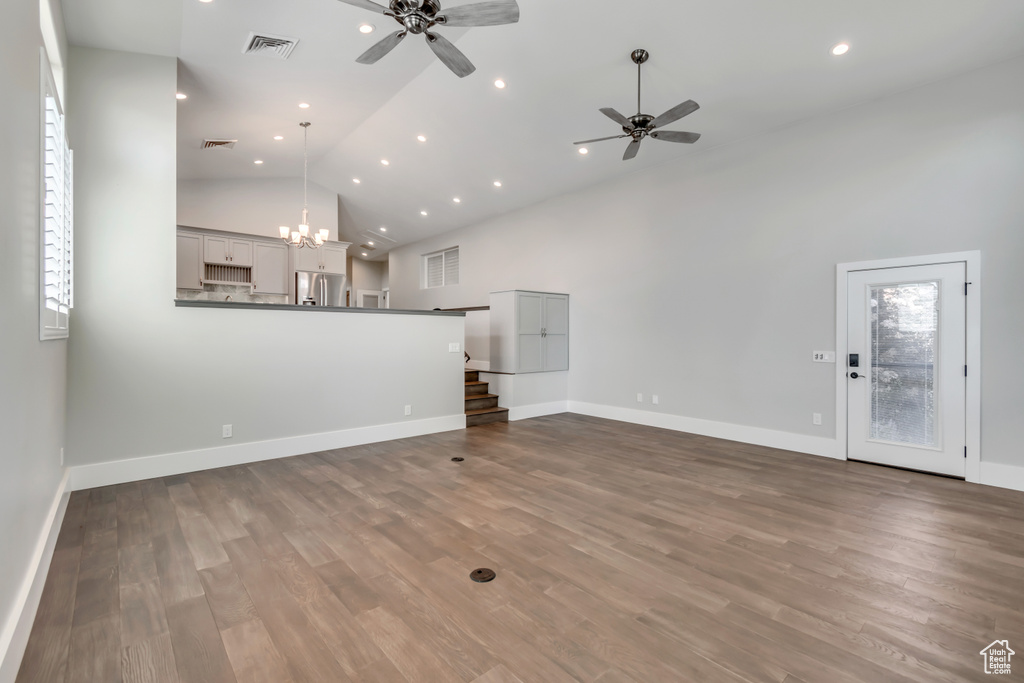 Unfurnished living room with ceiling fan, a chandelier, high vaulted ceiling, wood finished floors, and recessed lighting