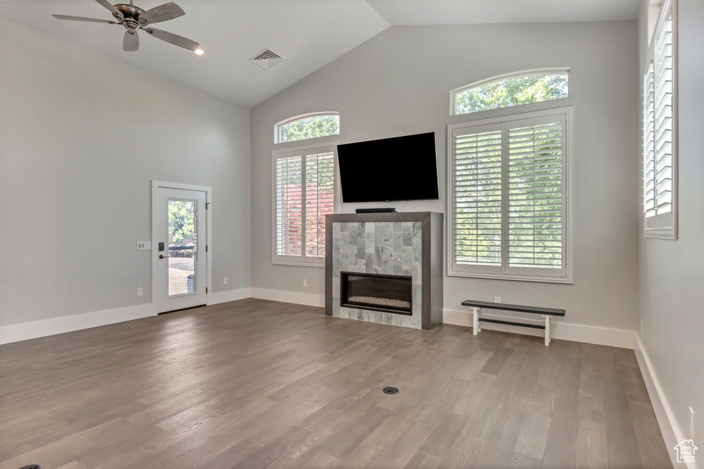 Unfurnished living room featuring ceiling fan, a tile fireplace, wood finished floors, baseboards, and high vaulted ceiling