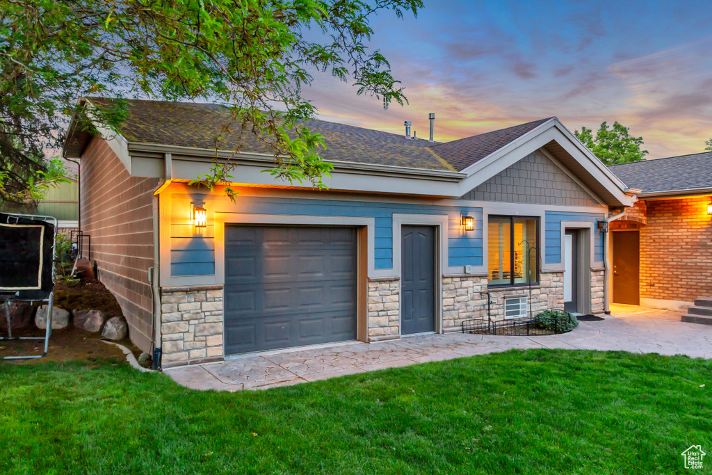View of front facade with stone siding, a shingled roof, a lawn, and an attached garage