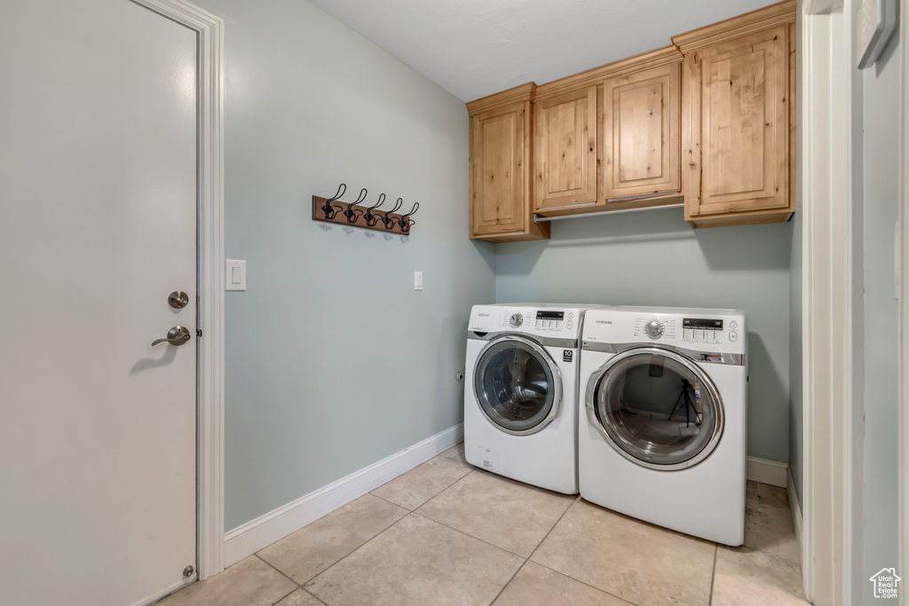 Laundry room with cabinet space, washing machine and dryer, light tile patterned flooring, and baseboards