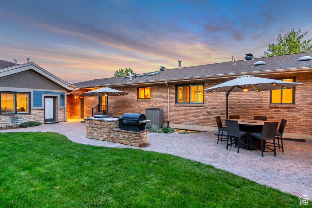 Back of property at dusk featuring a patio area, a yard, and central AC