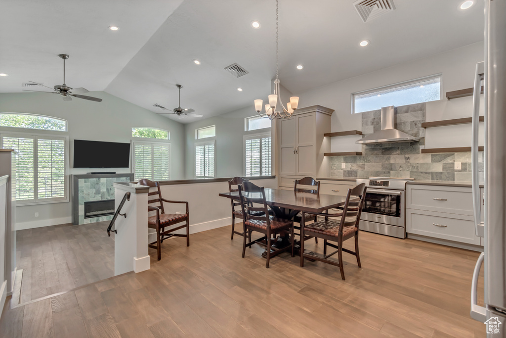 Dining area featuring light wood-style floors, lofted ceiling, a ceiling fan, a tiled fireplace, and baseboards