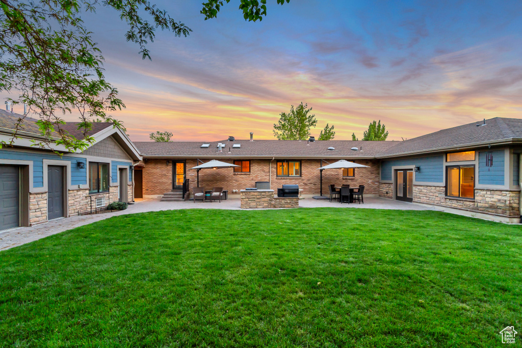 Back of property at dusk featuring entry steps, a patio area, a yard, and stone siding