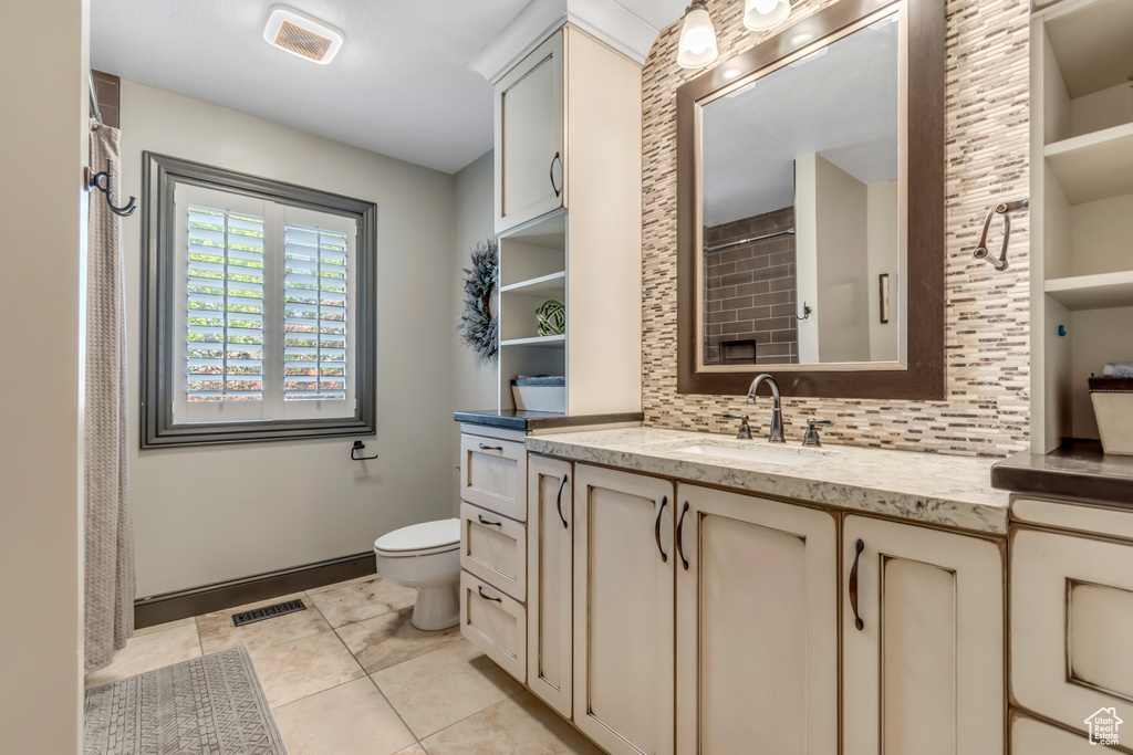 Bathroom featuring tasteful backsplash, toilet, vanity, tile patterned flooring, and curtained shower