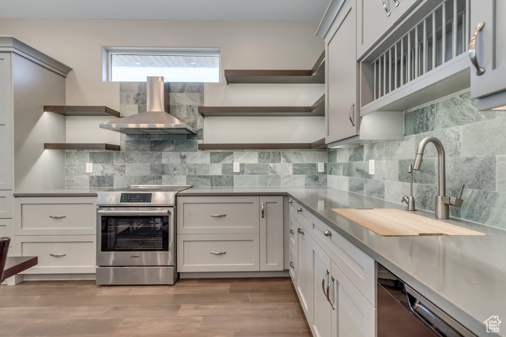 Kitchen with open shelves, electric stove, dishwashing machine, a sink, and wall chimney range hood