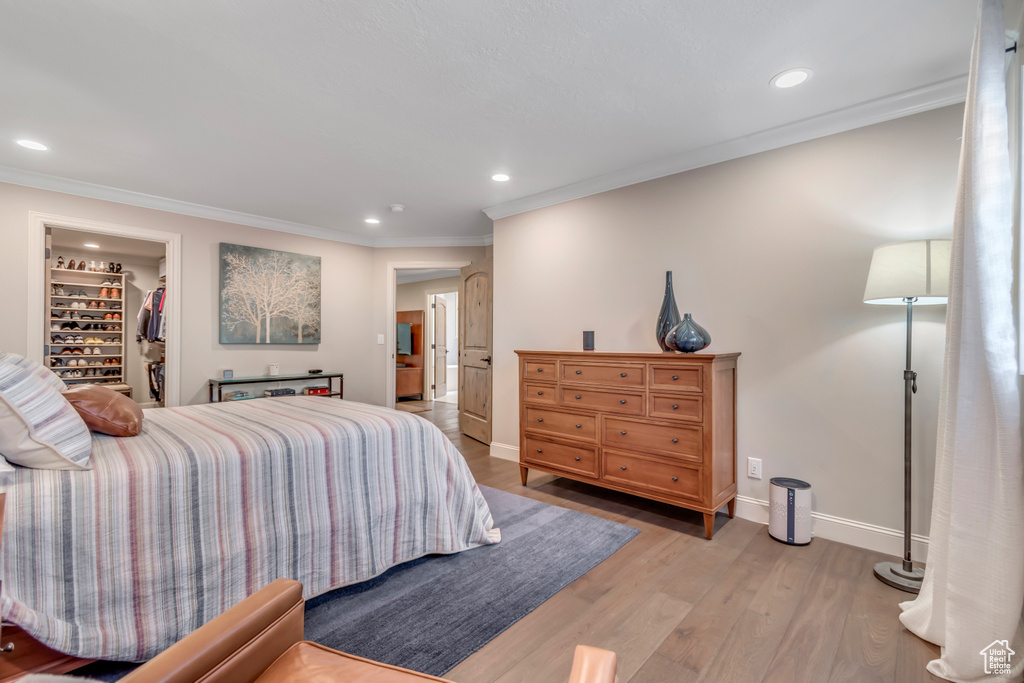 Bedroom featuring baseboards, ornamental molding, light wood-style flooring, recessed lighting, and a walk in closet