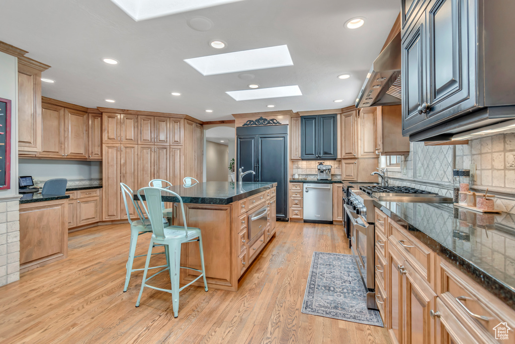 Kitchen featuring high end appliances, a skylight, light wood-style floors, a kitchen bar, and decorative backsplash