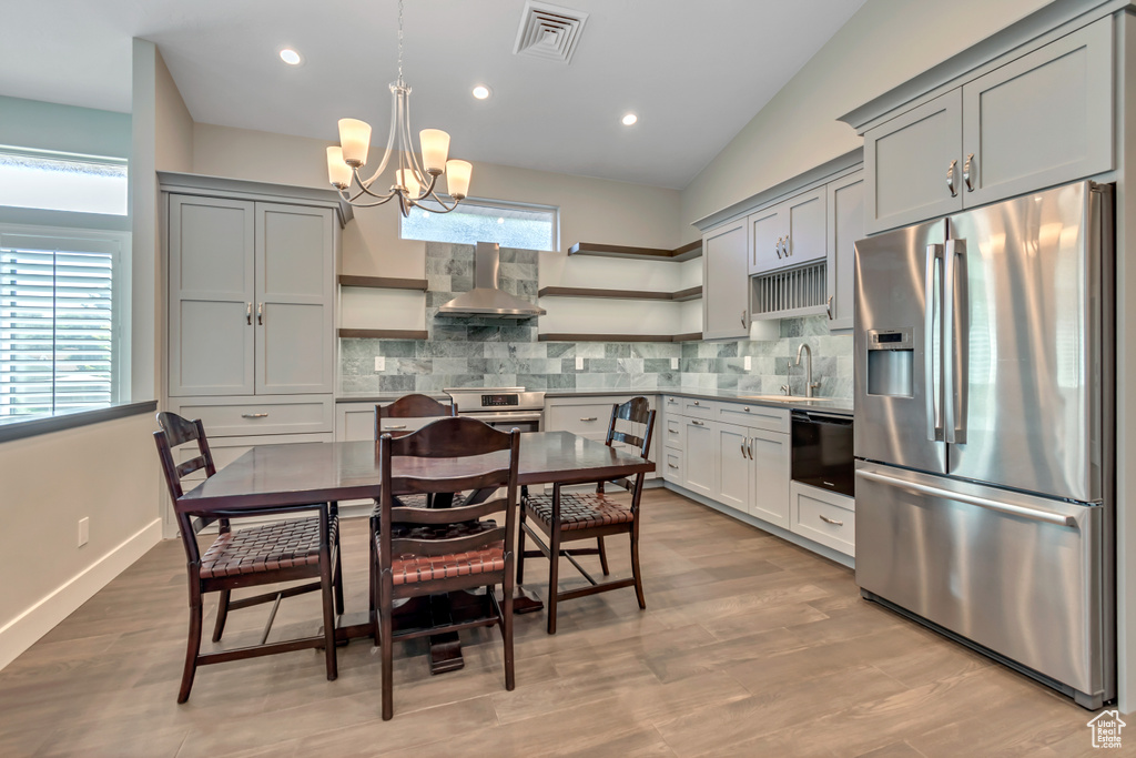 Kitchen featuring stainless steel appliances, open shelves, wall chimney exhaust hood, a sink, and lofted ceiling