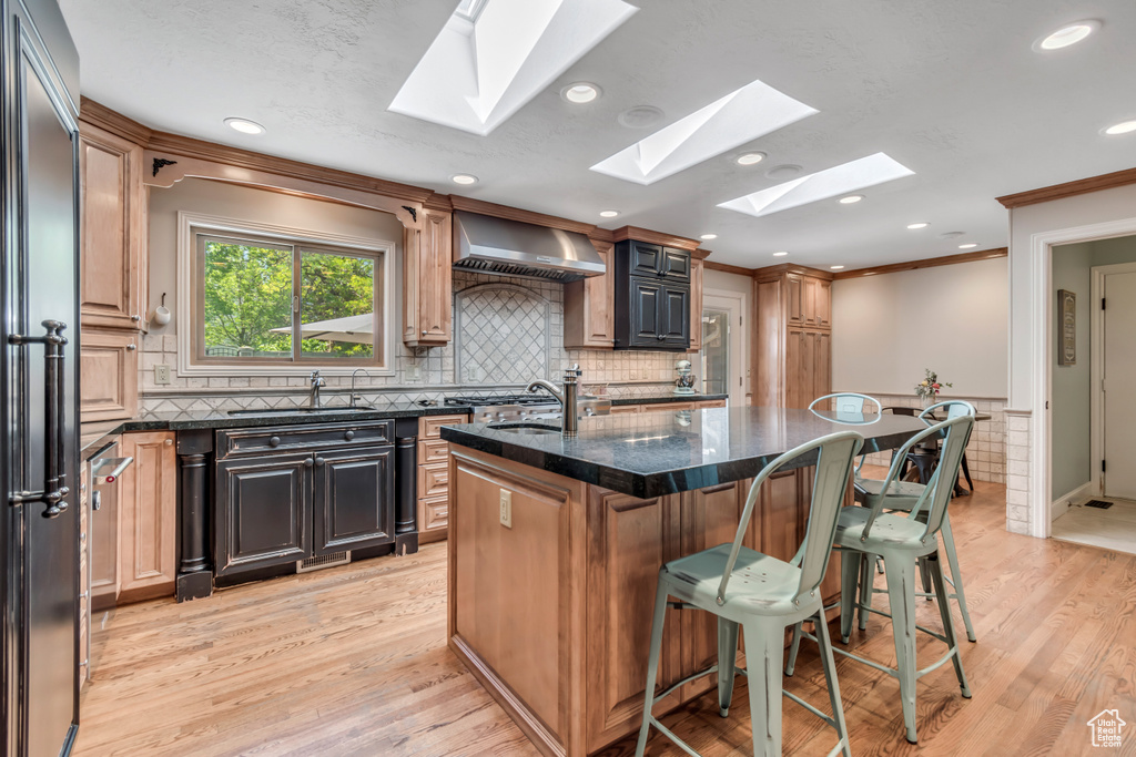 Kitchen with a skylight, wall chimney range hood, a sink, a kitchen breakfast bar, and light wood-style flooring