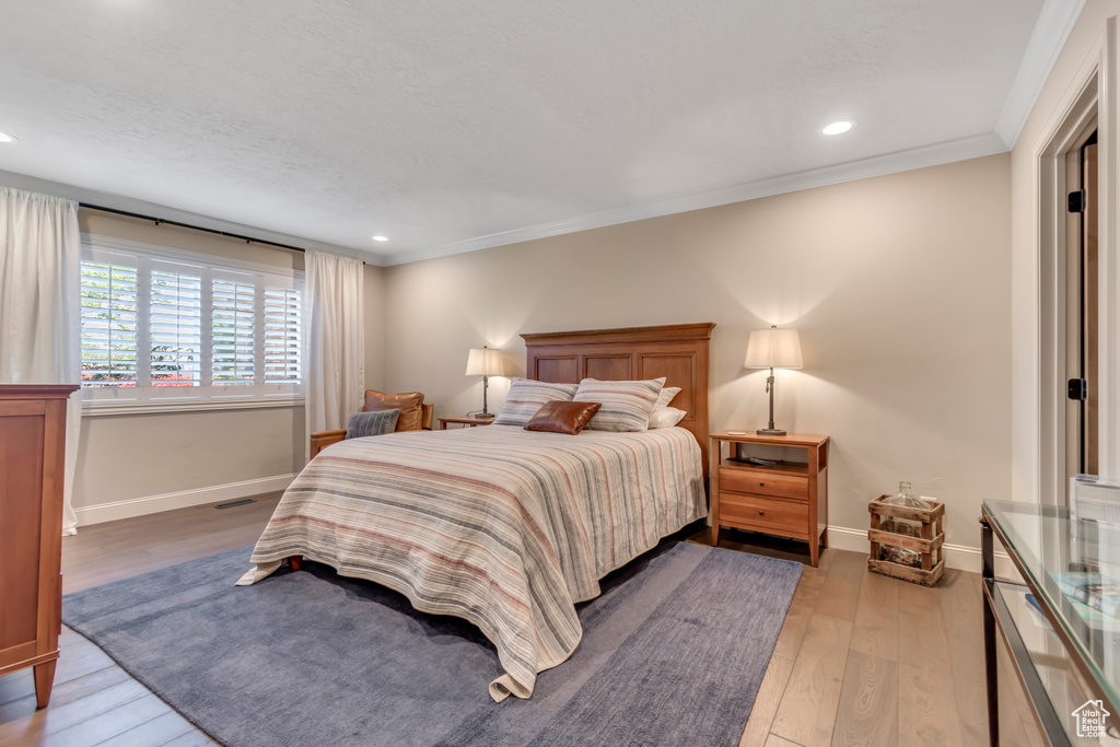 Bedroom with light wood finished floors, baseboards, crown molding, and recessed lighting