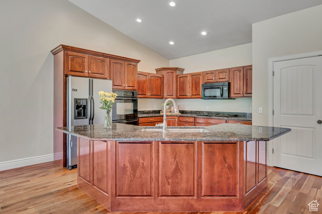 Kitchen with a sink, black appliances, dark stone countertops, light wood-style flooring, and high vaulted ceiling