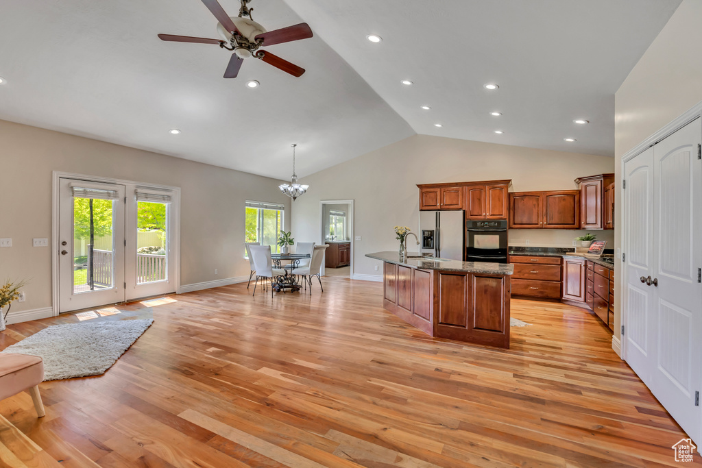 Kitchen featuring light wood-style floors, brown cabinetry, stainless steel fridge with ice dispenser, a chandelier, and a center island with sink