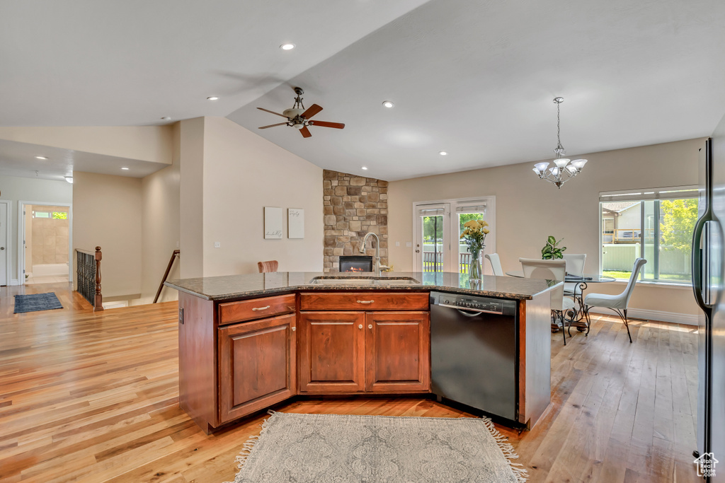 Kitchen featuring dishwashing machine, a sink, light wood-style flooring, a center island with sink, and lofted ceiling