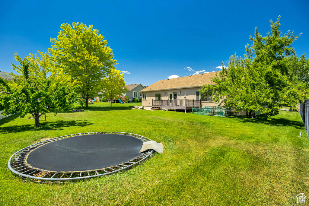 View of green lawn featuring a trampoline and a wooden deck