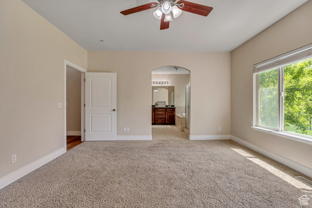 Unfurnished bedroom featuring arched walkways, light colored carpet, baseboards, and ensuite bath