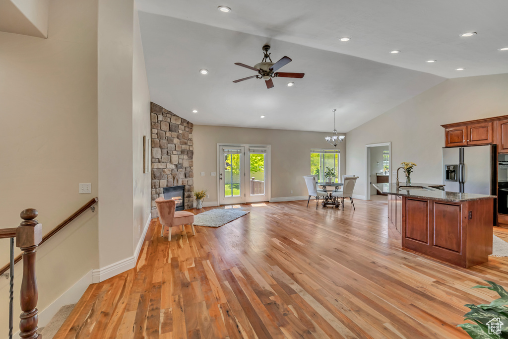 Living area with light wood-style floors, ceiling fan, a fireplace, a chandelier, and high vaulted ceiling
