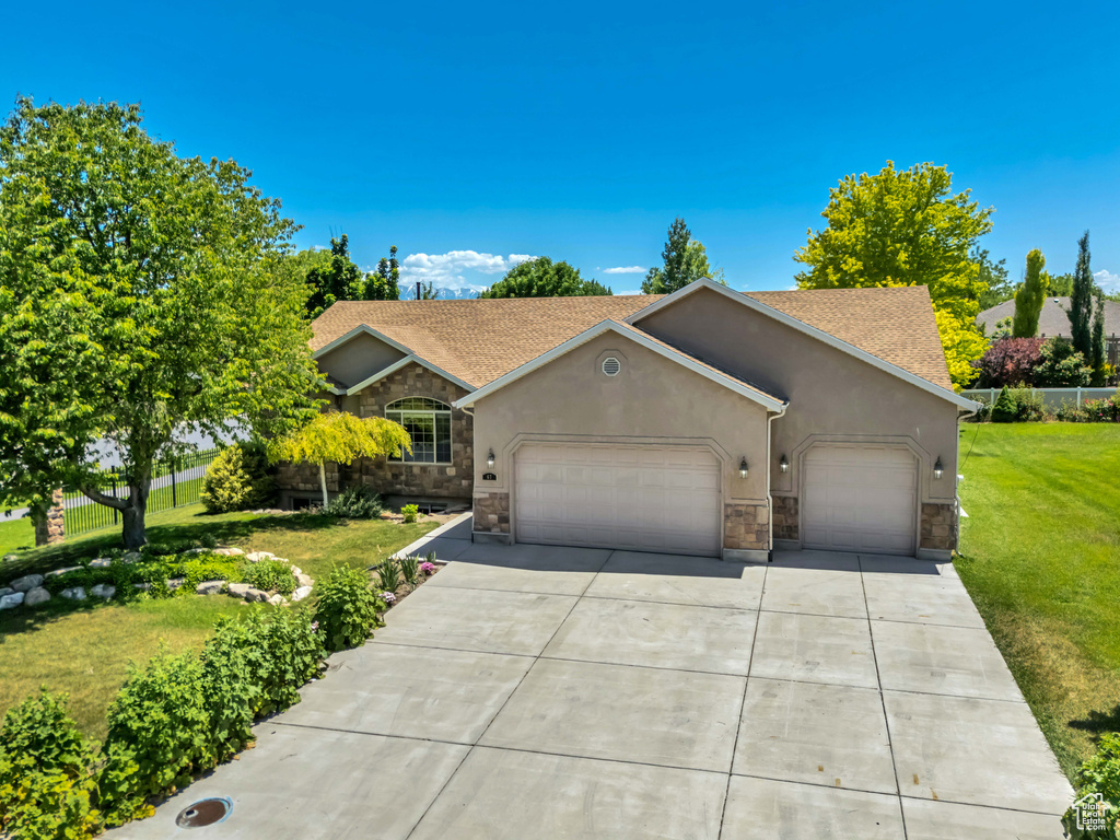 View of front of house featuring stone siding, an attached garage, stucco siding, a front lawn, and concrete driveway