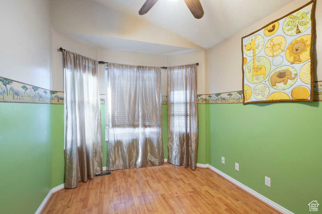 Unfurnished room featuring vaulted ceiling, plenty of natural light, ceiling fan, wood finished floors, and baseboards