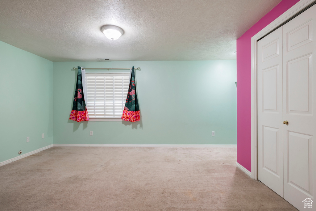 Empty room with a textured ceiling, carpet floors, and baseboards