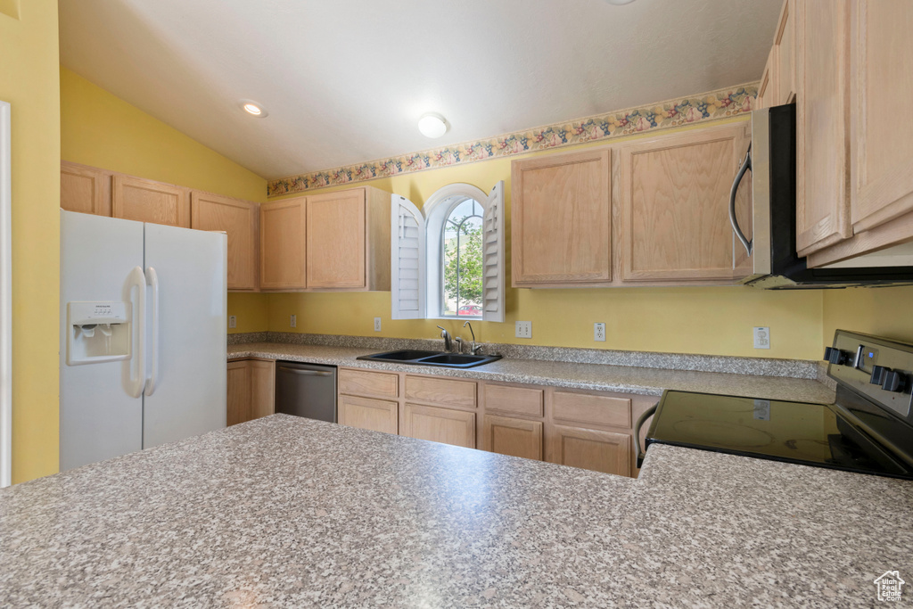 Kitchen with stainless steel appliances, light brown cabinetry, a sink, lofted ceiling, and light countertops