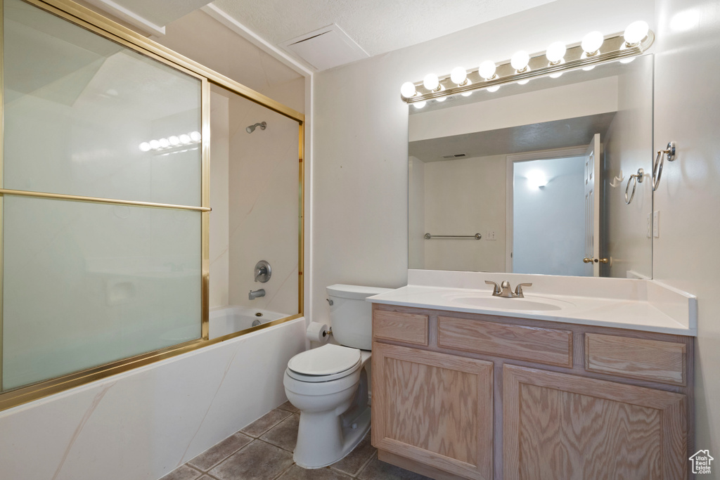 Bathroom with toilet, vanity, shower / bath combination with glass door, and tile patterned floors