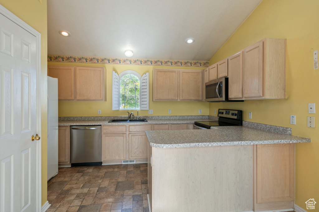 Kitchen with appliances with stainless steel finishes, light brown cabinetry, a sink, a peninsula, and dark stone finish flooring