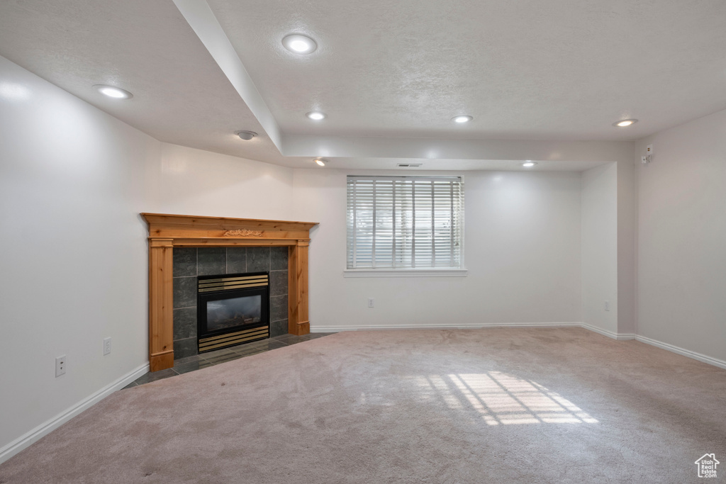 Unfurnished living room featuring carpet floors, recessed lighting, a tile fireplace, and baseboards
