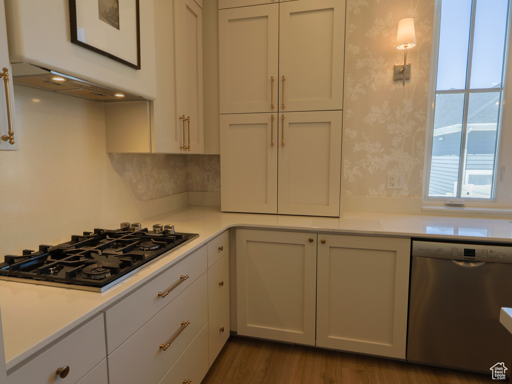 Kitchen with stainless steel dishwasher, black gas cooktop, light countertops, wallpapered walls, and white cabinets