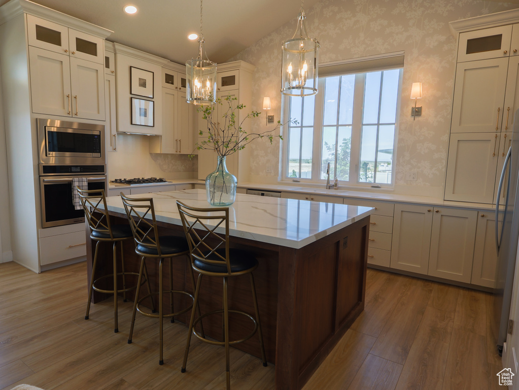 Kitchen with appliances with stainless steel finishes, a chandelier, wood finished floors, a kitchen island, and recessed lighting